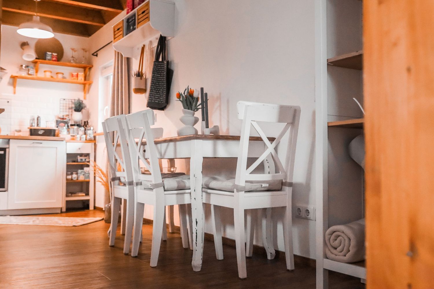 White dining table and chairs in a cozy kitchen with hardwood floors and warm lighting.