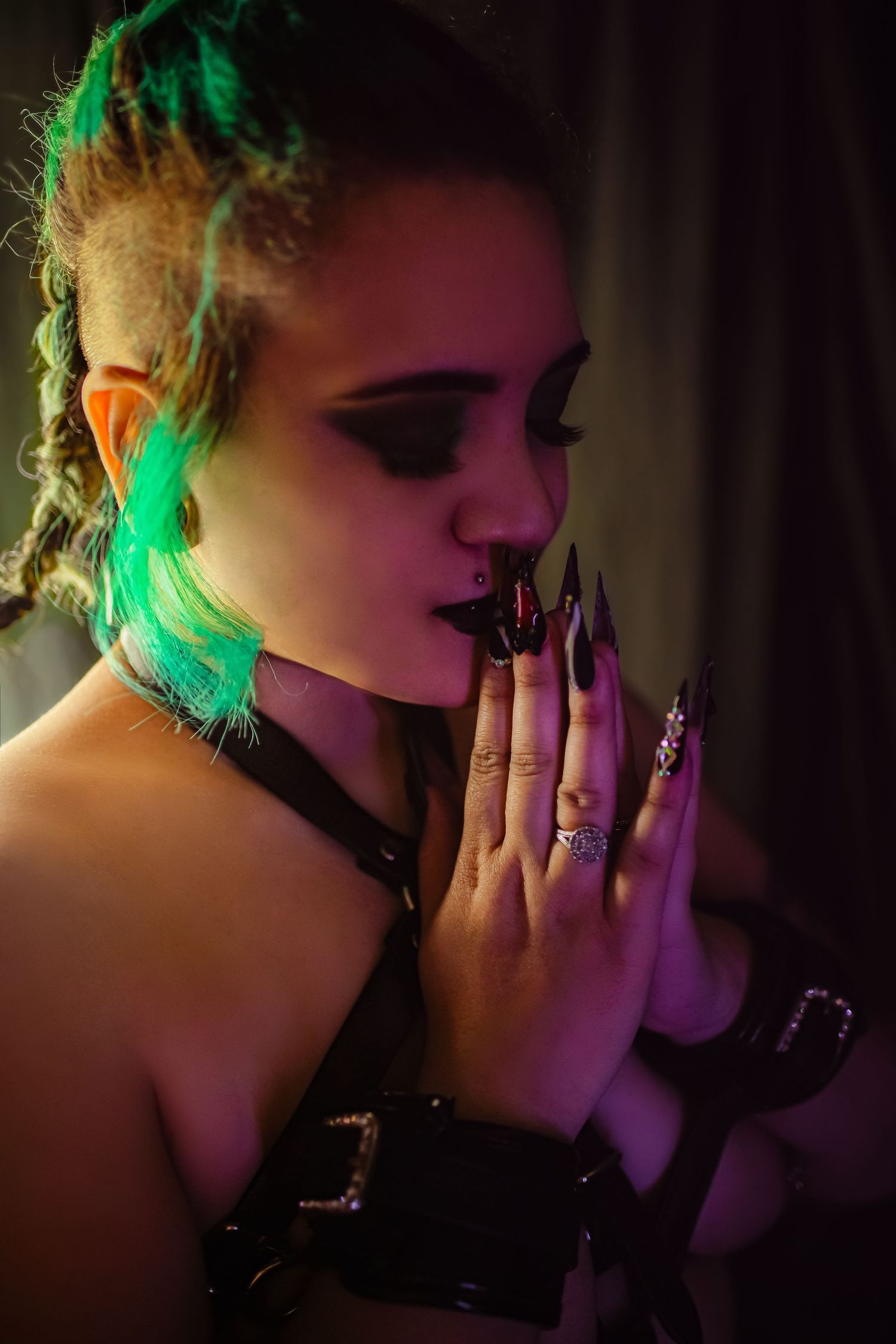 A gothic woman with green dreadlocks, black nails, and dark makeup poses dramatically in purple neon light.