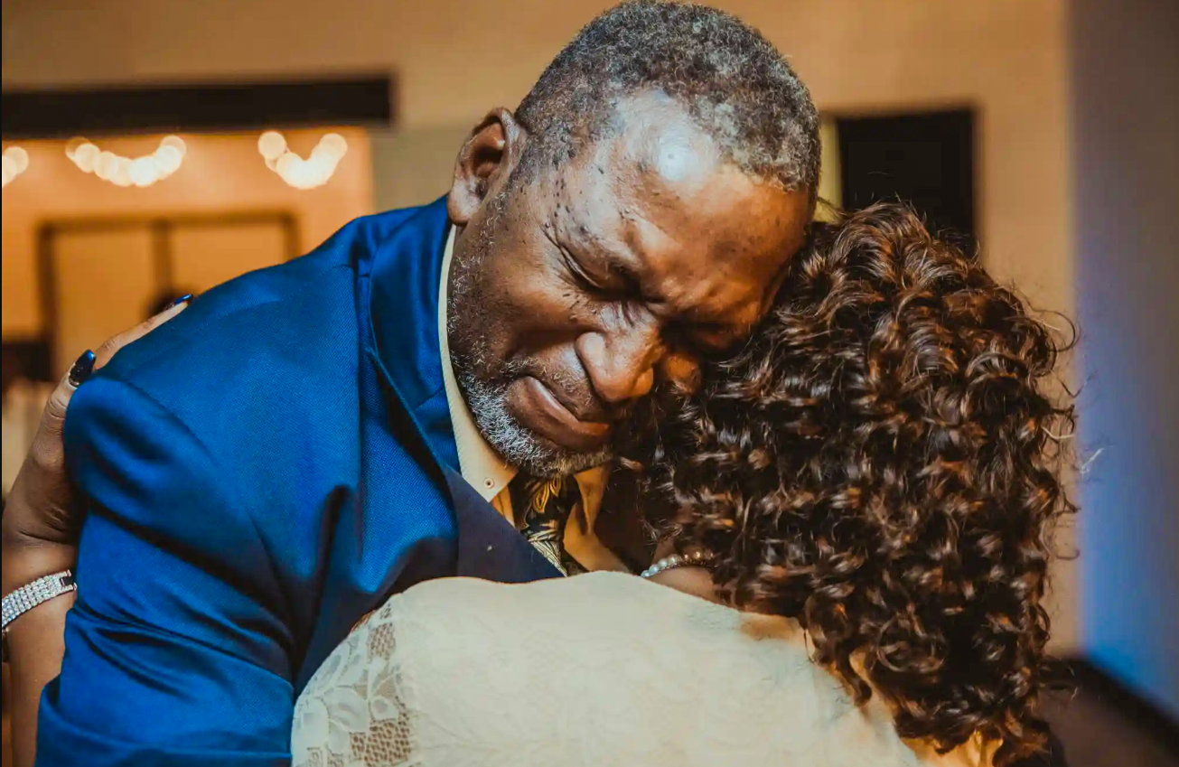 Emotional father-daughter dance at wedding, man in blue suit embracing bride in heartfelt moment.