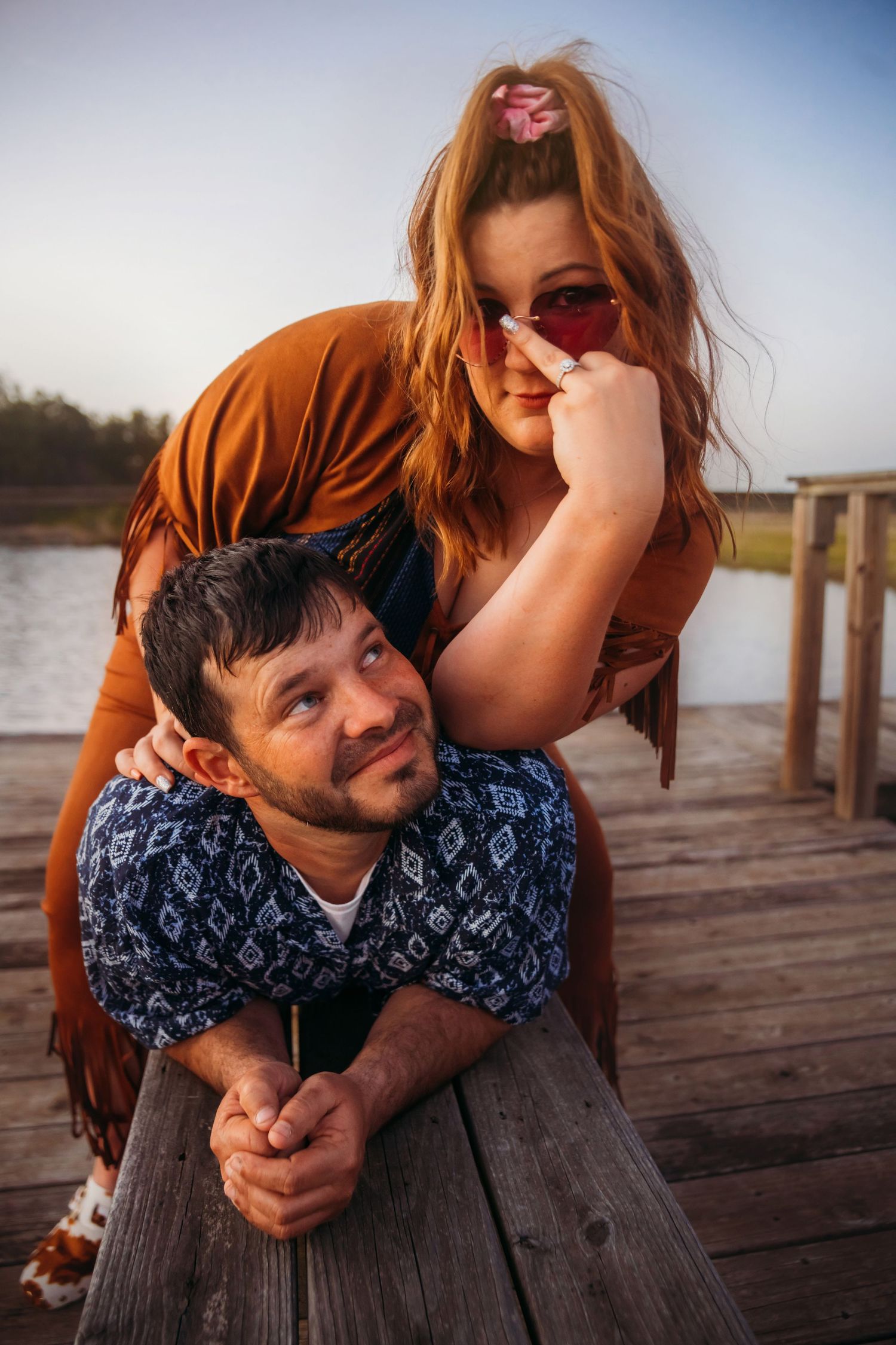 Affectionate couple posing on a wooden dock by a lake during golden hour sunset.