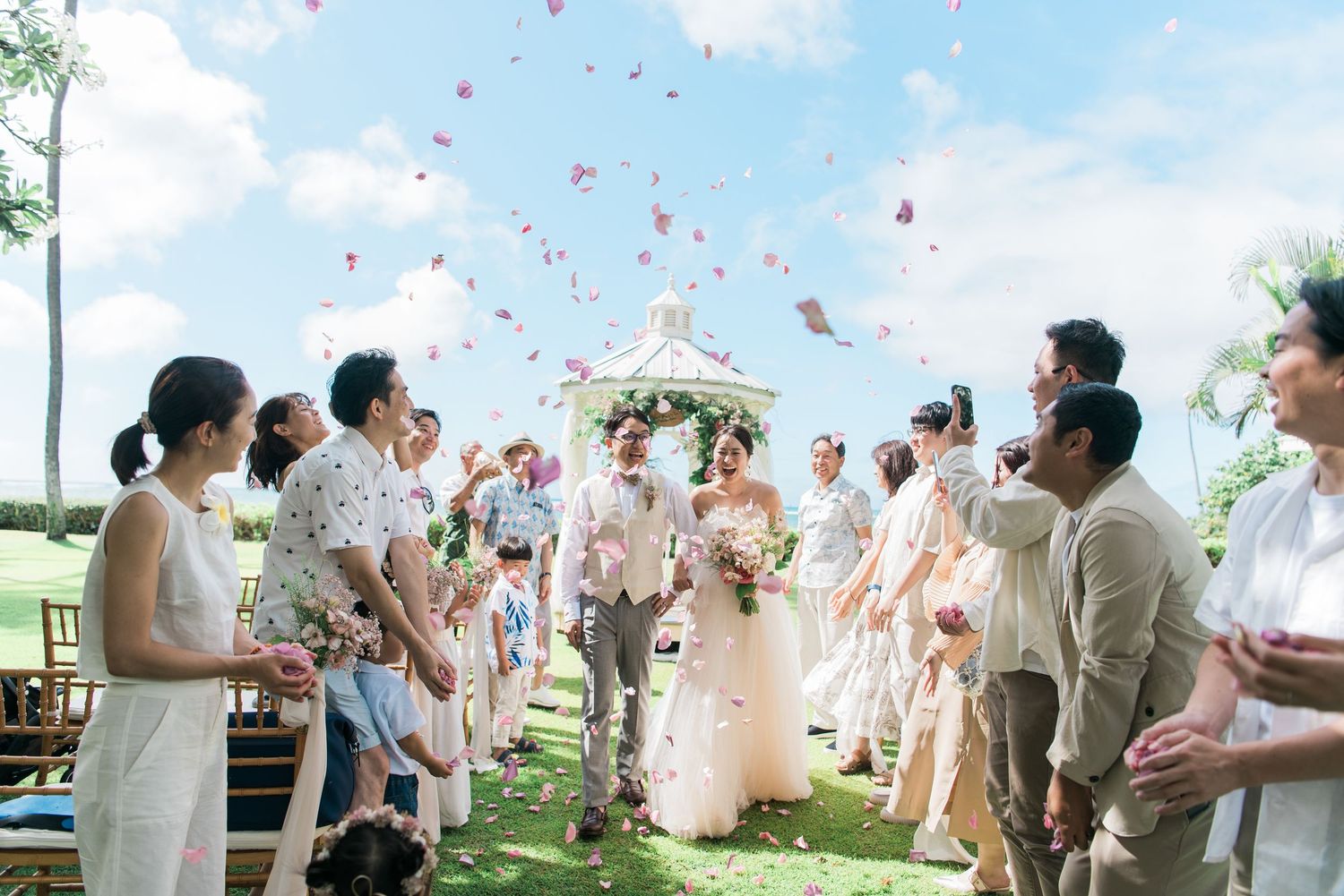 Newlywed couple celebrating with guests and flower petals at a Hawaii wedding