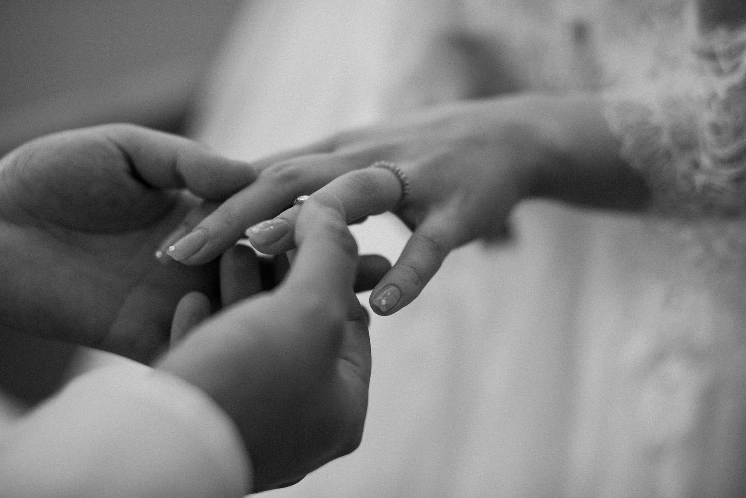 Black and white close-up of a groom placing a wedding ring on the bride’s finger