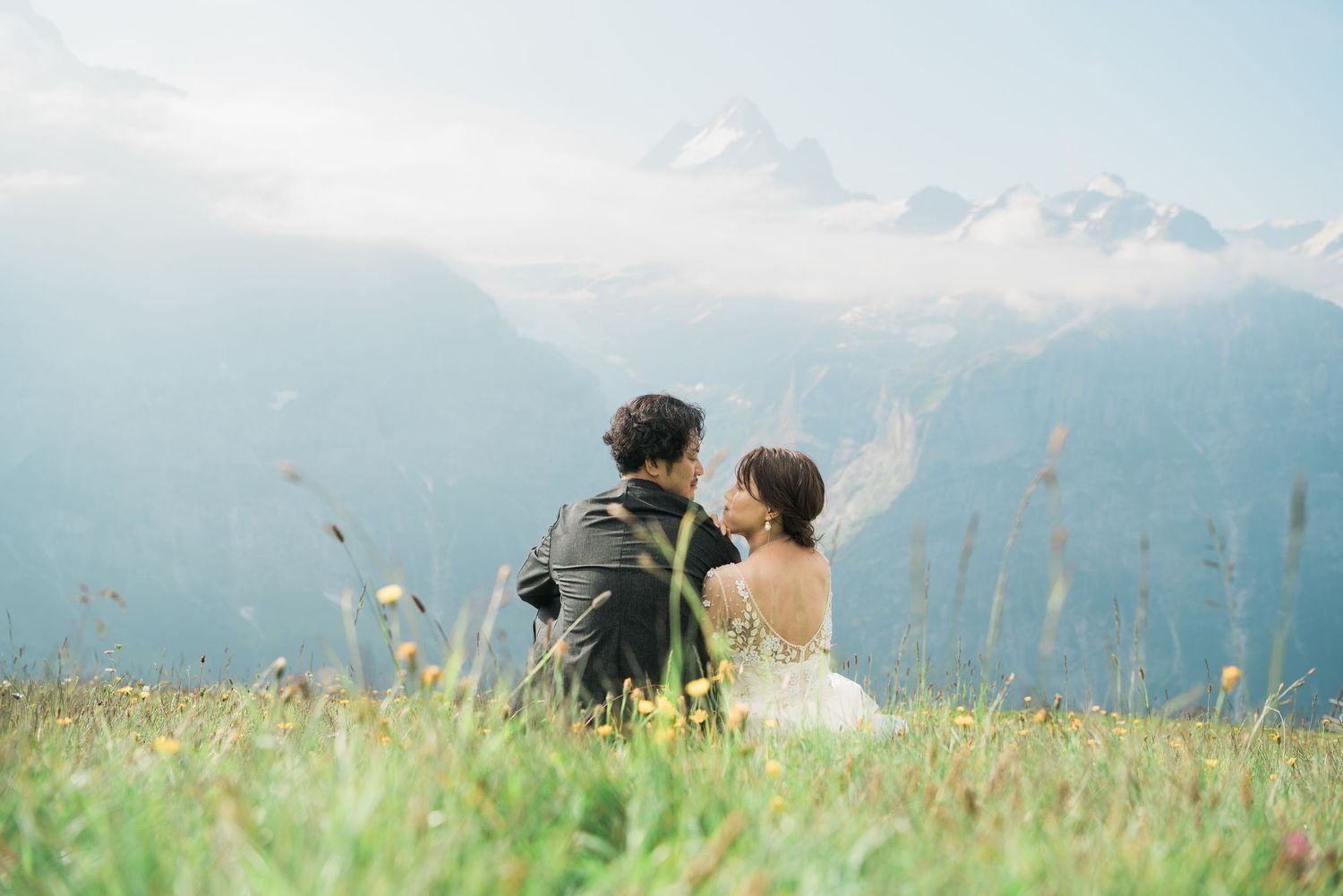 Newlywed couple sitting together in a meadow overlooking the Swiss Alps