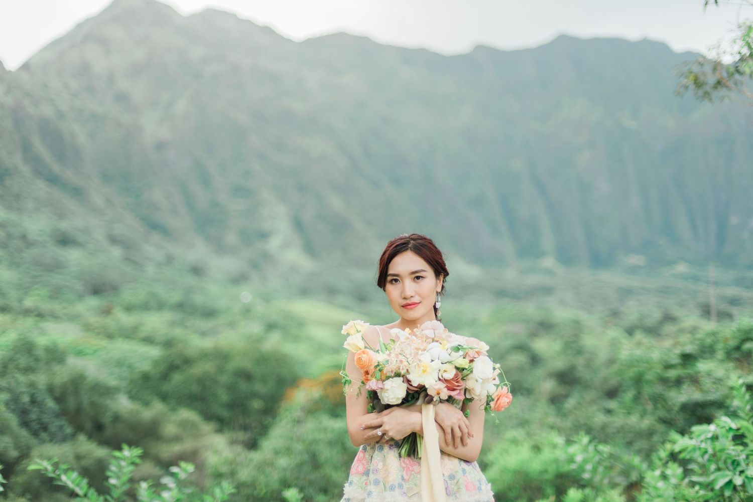 Bride holding her bouquet with lush green mountains in Oahu, Hawaii