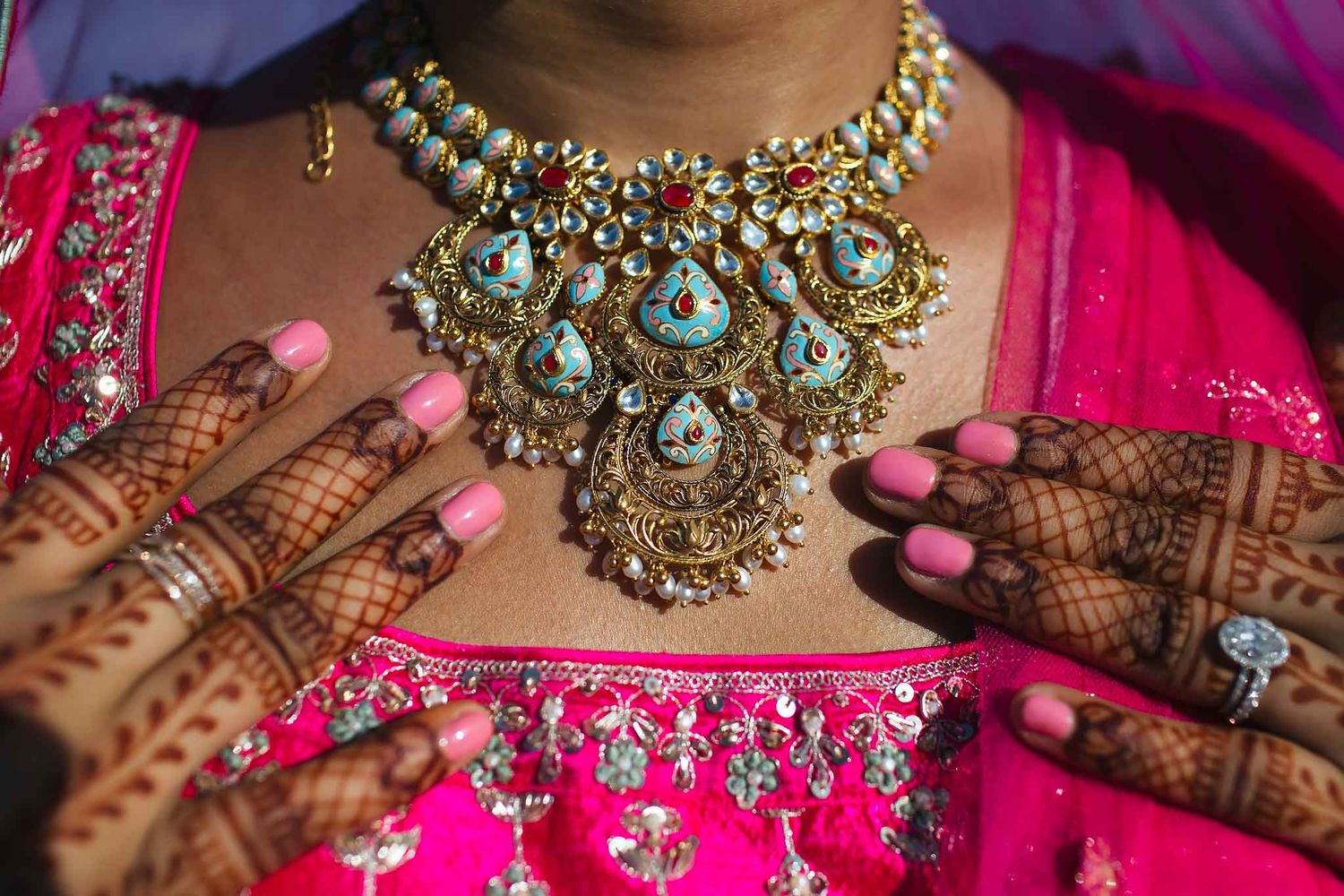 Close-up of Indian bridal jewelry, mehndi hands, and pink traditional attire during luxury Hindu wedding celebration.