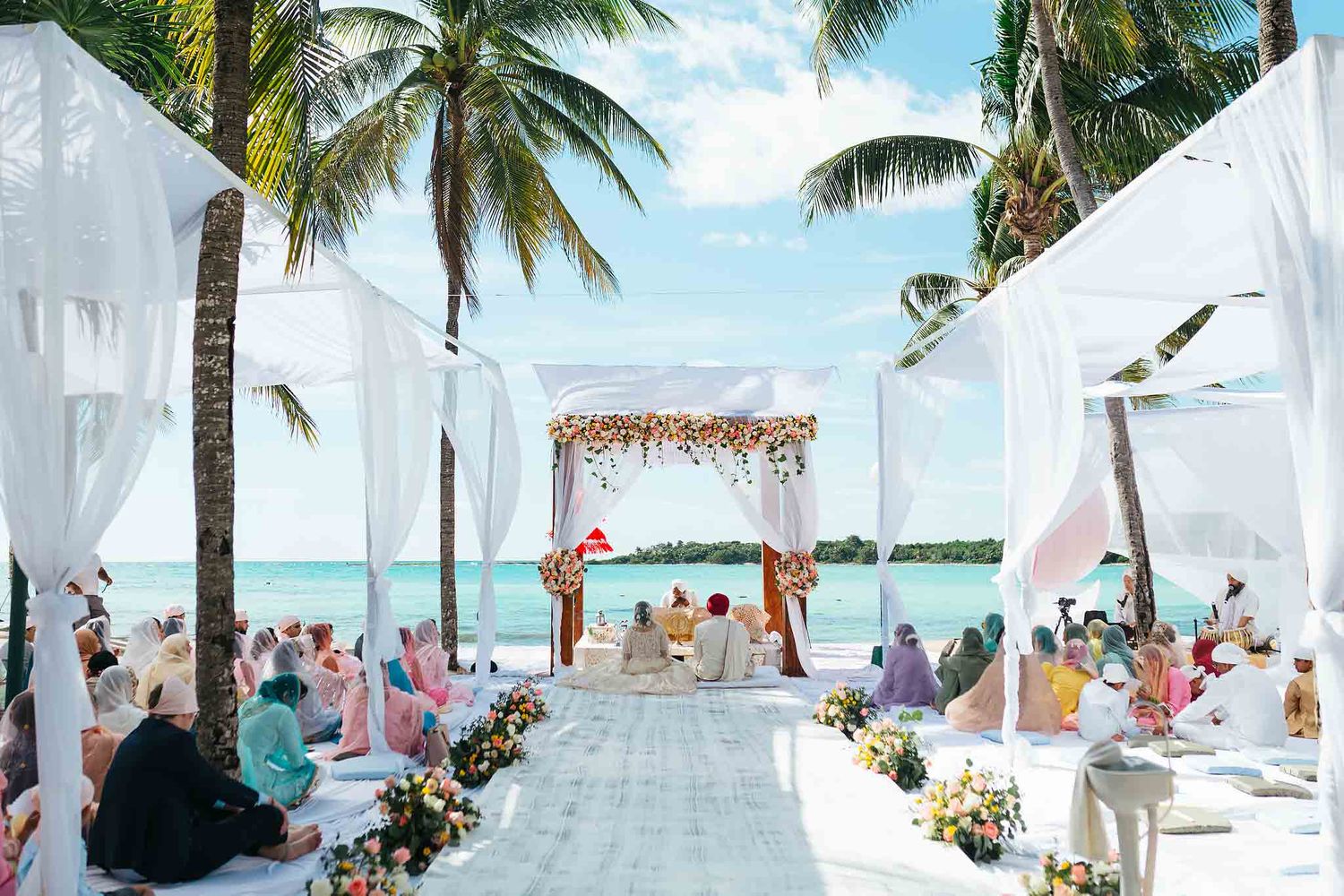 Luxury Indian Hindu beach wedding ceremony at Barcelo Riviera Maya with oceanfront mandap, tropical palm trees, floral decor, and guests dur