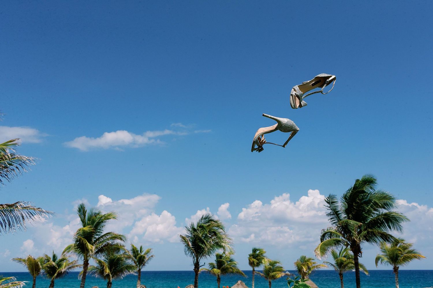 Bride’s sparkling wedding shoes tossed into the air above palm trees and the Caribbean Sea during preparations at UNICO 20°87° Hotel Riviera