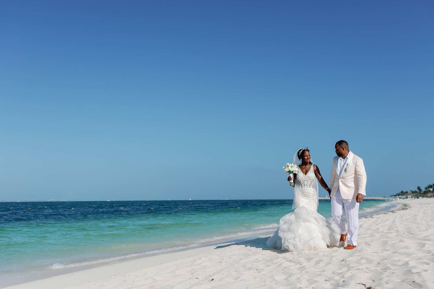 Bride and groom walking along the white sand beach at Finest Playa Mujeres in Costa Mujeres during a destination wedding photography session