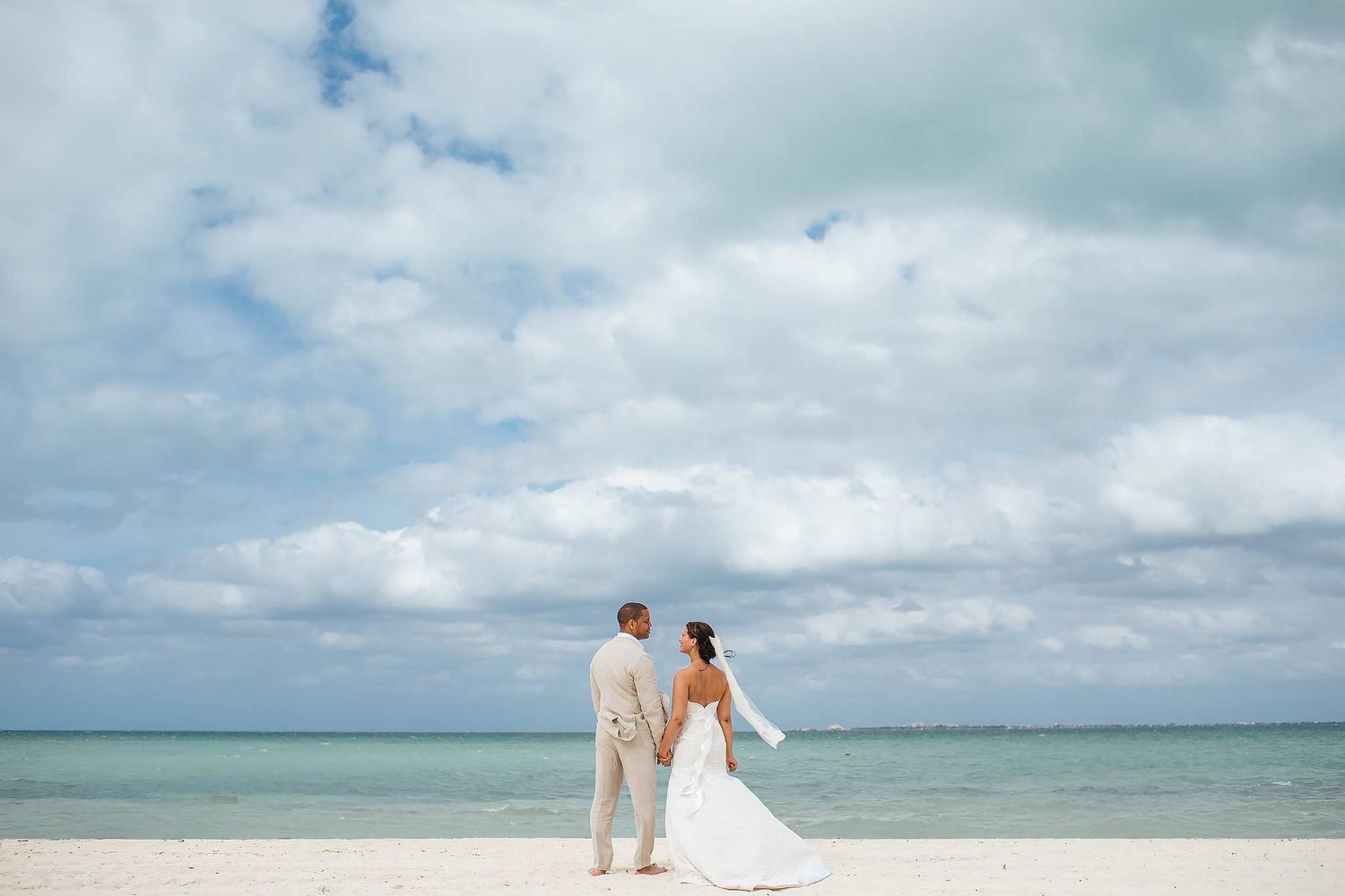 Bride and groom standing on the beach at Excellence Playa Mujeres with turquoise Caribbean waters and dramatic clouds during a destination w
