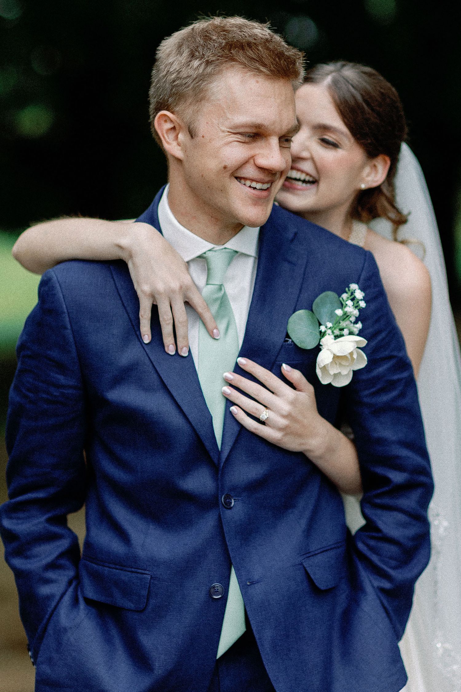 Kaylee hugging Joseph from behind as they laugh during their wedding portraits at Mayowood Stone Barn in Rochester, Minnesota.