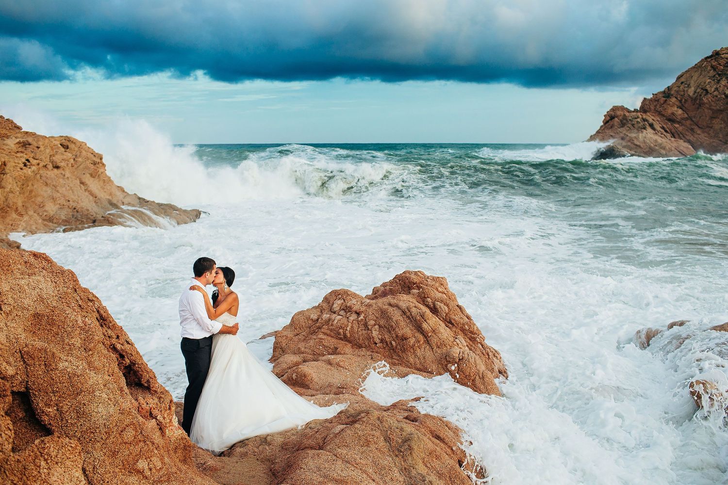 Luxury destination wedding portrait at Chileno Bay Resort in Los Cabos with crashing waves and dramatic Baja coastline scenery.