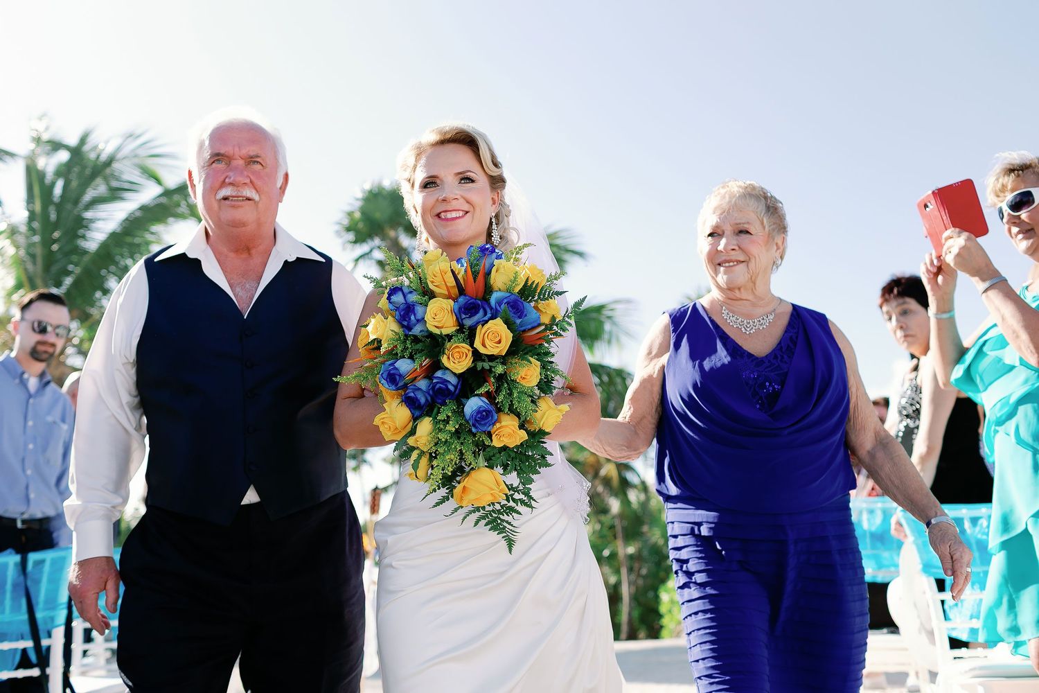 Carly smiling with two loved ones as she enters the beach ceremony