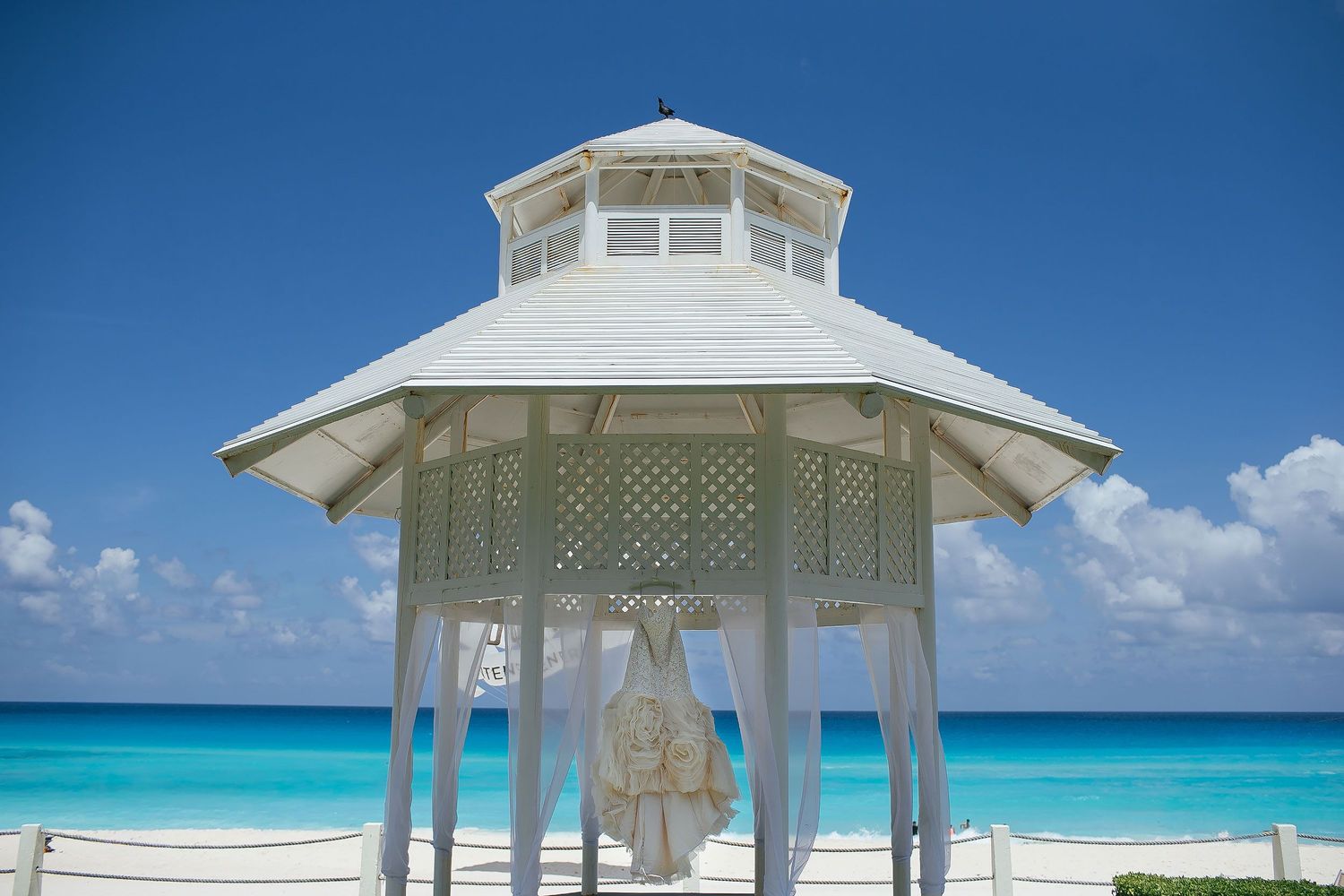Wedding gown hanging inside a white oceanfront gazebo overlooking the turquoise Caribbean Sea at Hotel Riu Palace Riviera Maya.