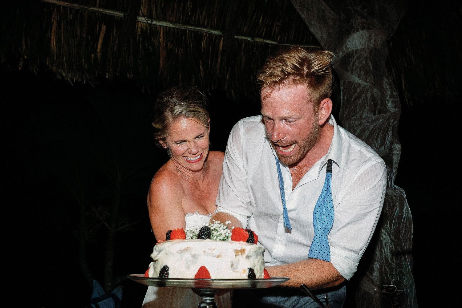 Cressida and Alan laughing as they cut their fruit-decorated wedding cake during their private Riviera Maya reception.