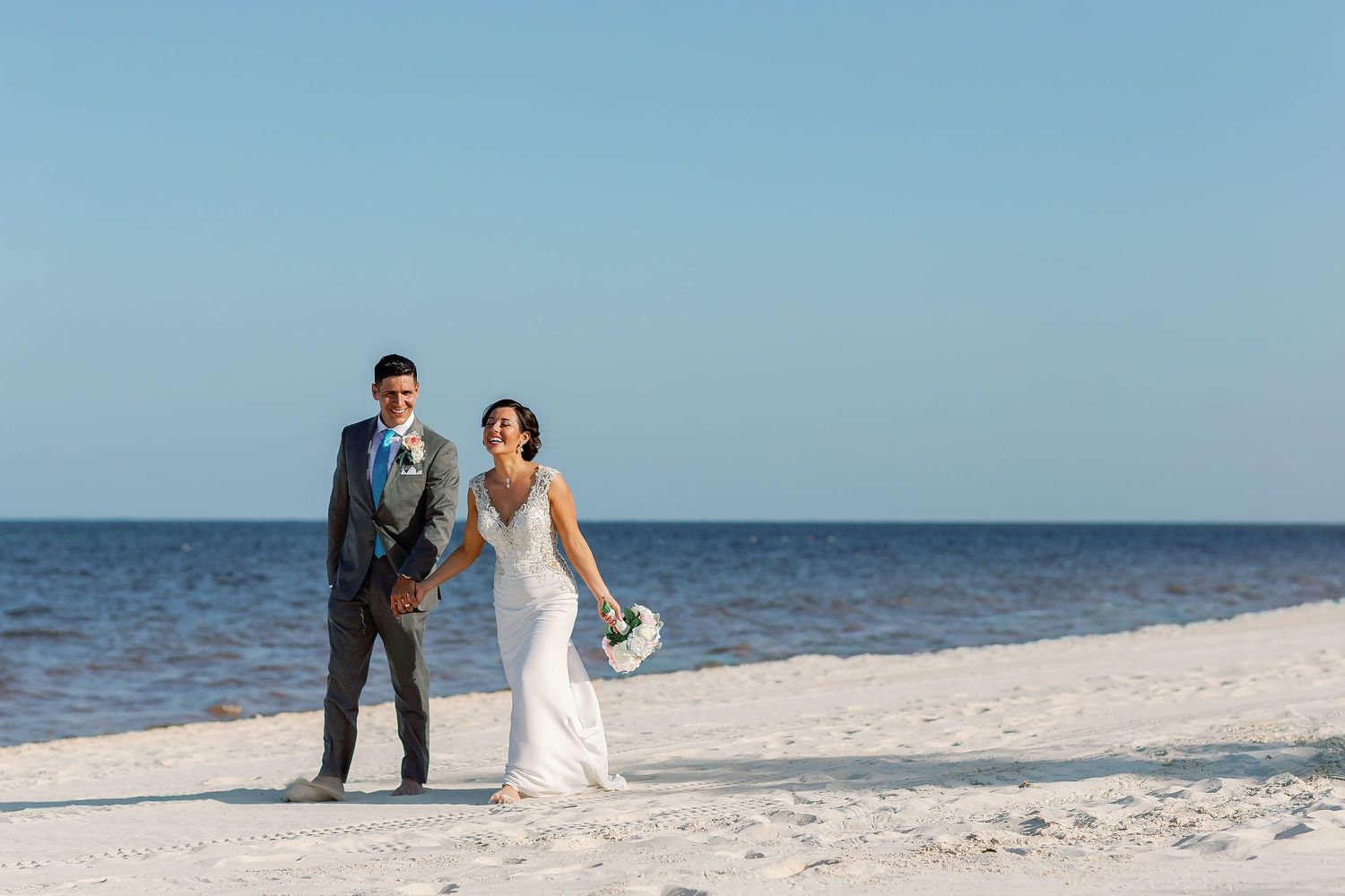 Bride and groom laughing and holding hands on the beach during their wedding portrait session at The Grand at Moon Palace Cancun.