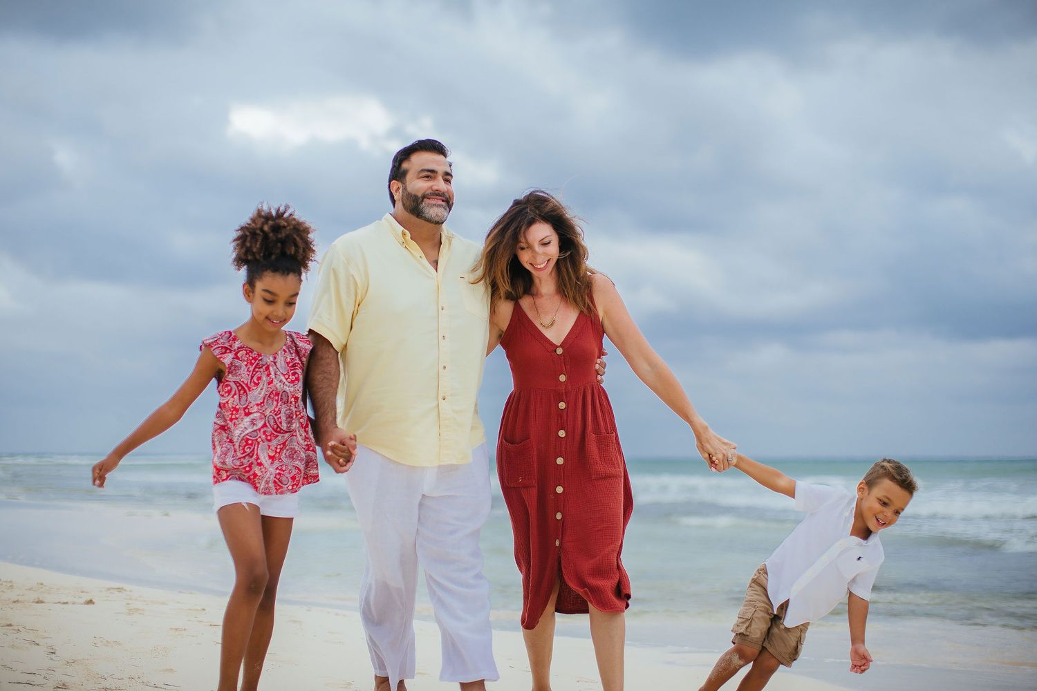 Family wearing coordinated neutral and warm-toned outfits during a beach photo session in Playa del Carmen, Riviera Maya.