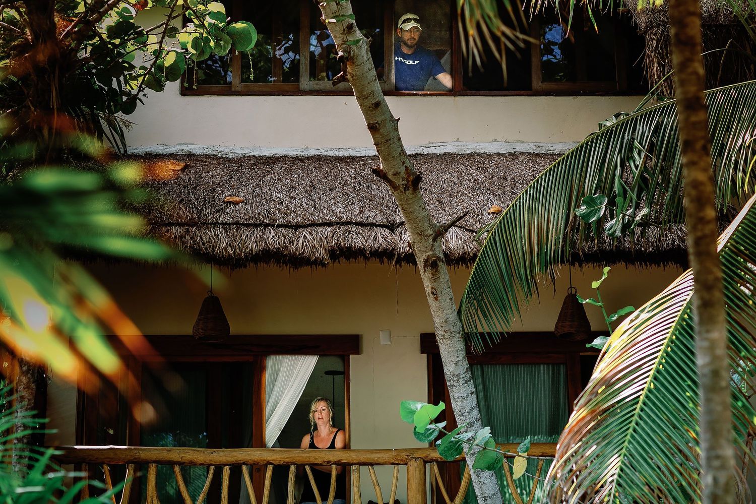 Matt stands at an upper window while Ashley looks out from the lower level of their private Tulum house.