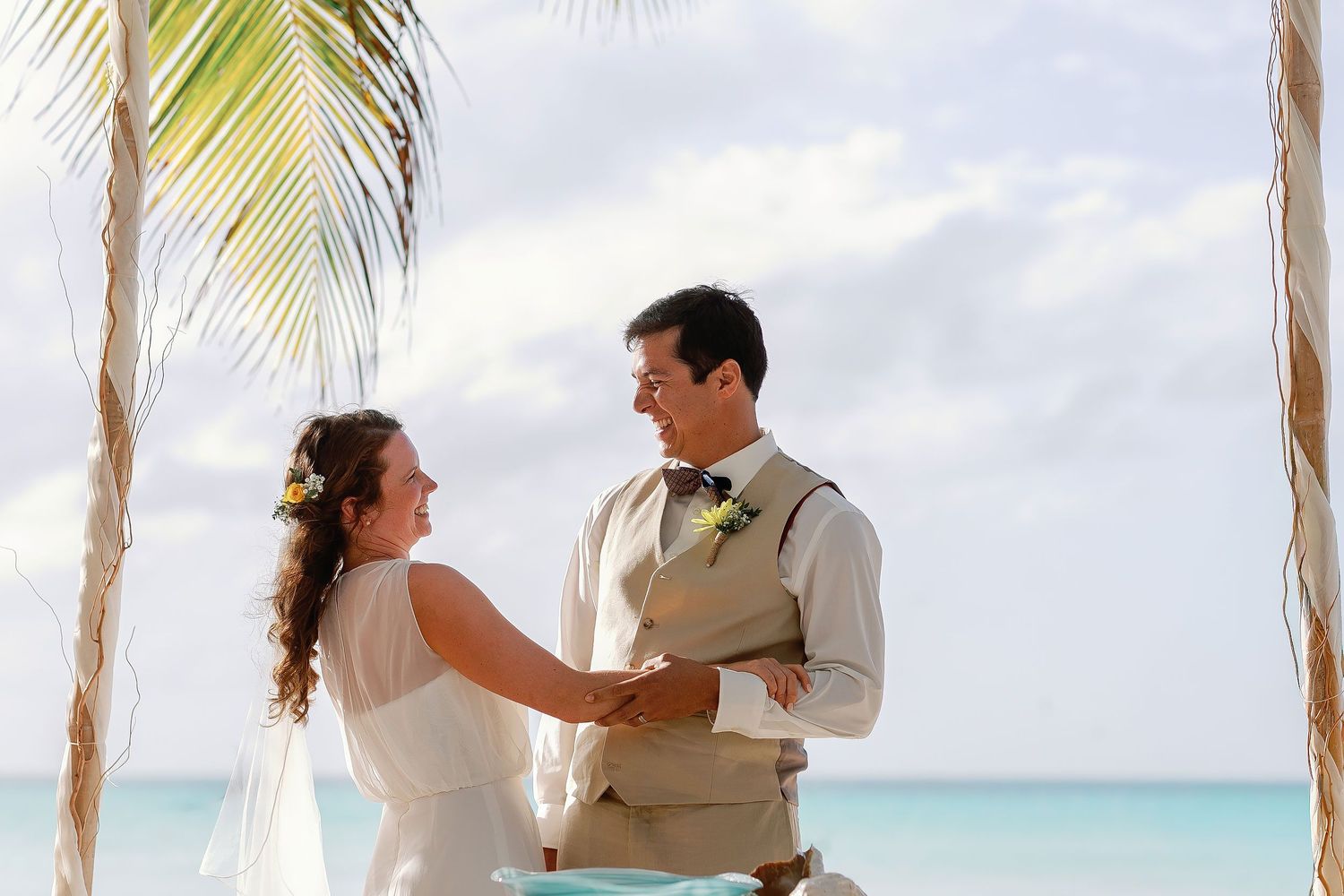 Li and Carlos laugh and hold hands beneath their beachfront ceremony canopy at Playa Norte.