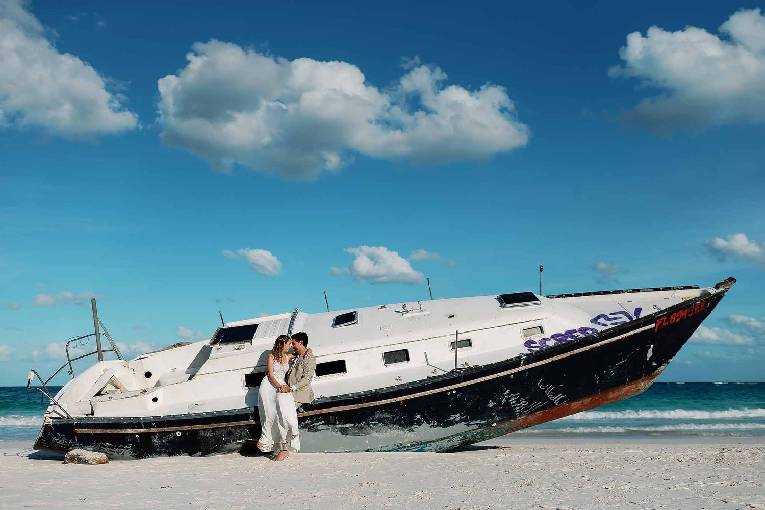 Romantic Cancun engagement photo session with couple embracing beside a boat on a white sand beach in the Riviera Maya