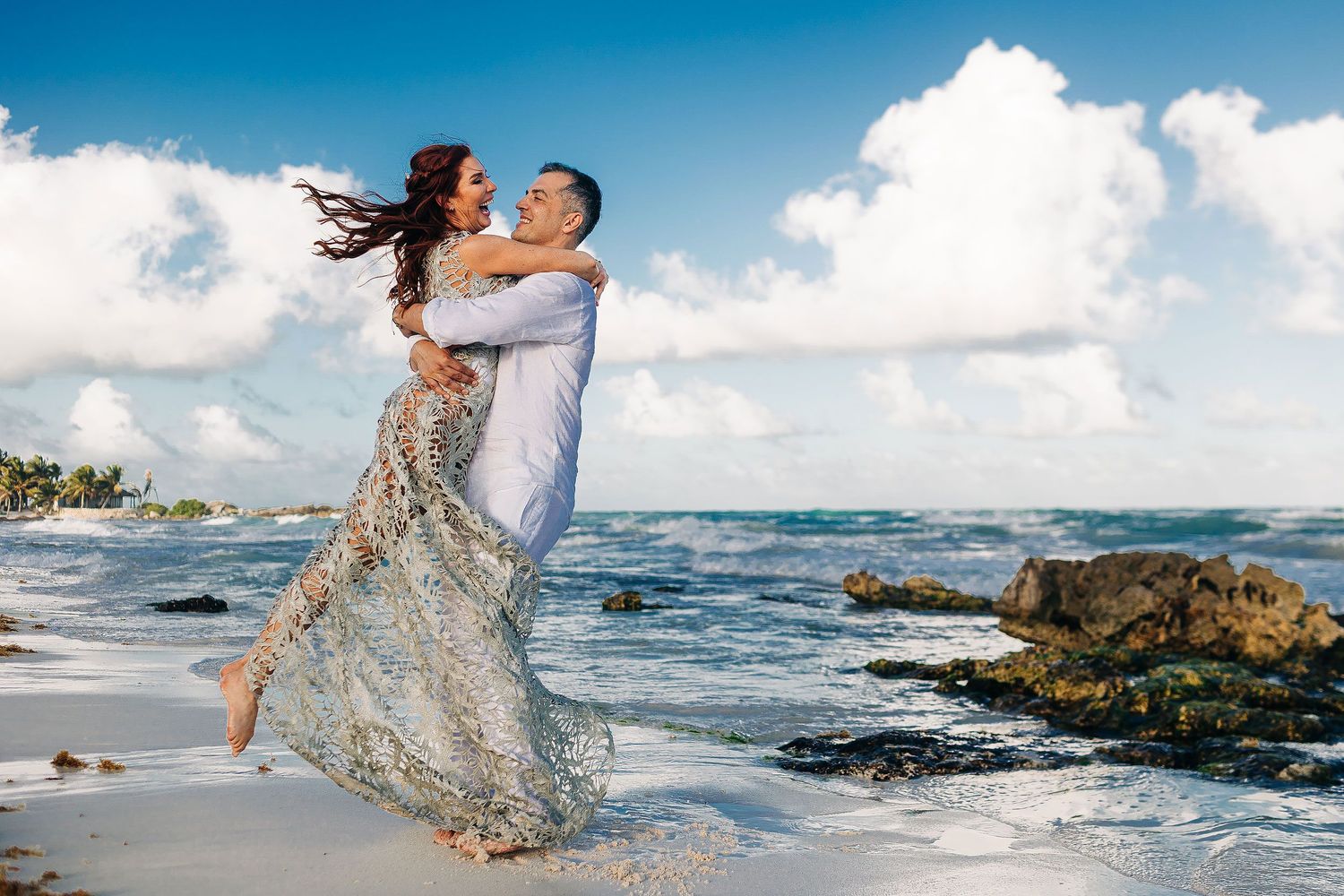 Evish lifts a laughing Sarah on the shoreline after their Tulum elopement.