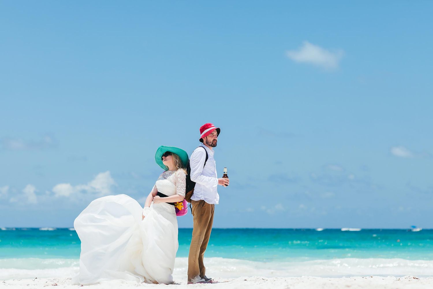 Couple in wedding attire posing on the beach at JW Marriott Cancun Resort & Spa, with turquoise ocean and clear blue sky, creative editorial