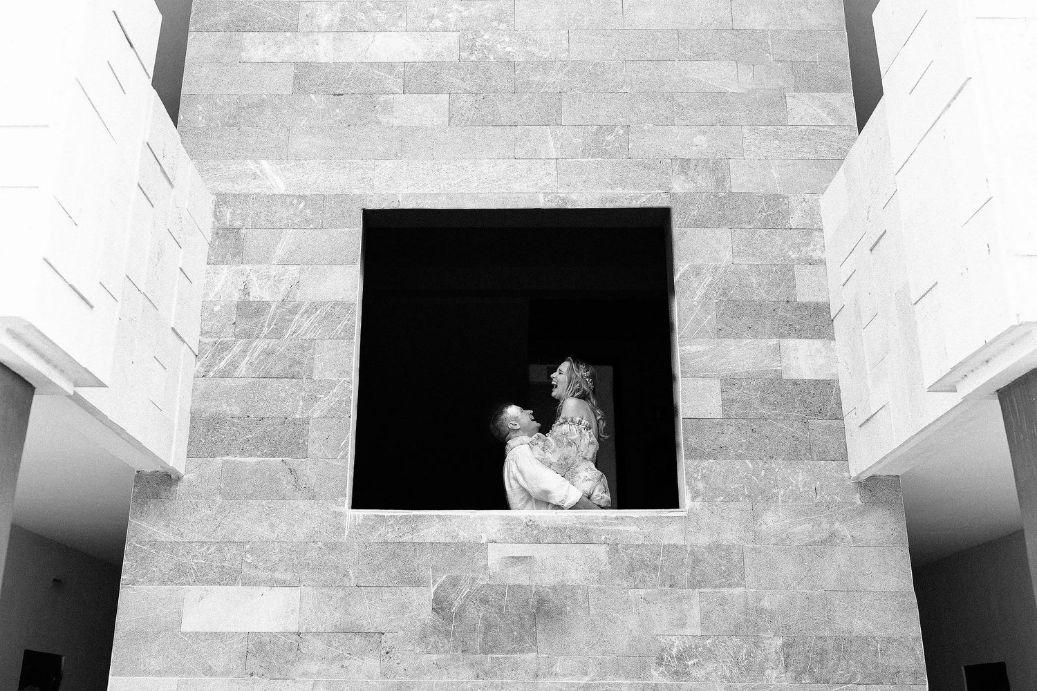 Black-and-white portrait of Autumn and Brian laughing inside the modern architecture of Dreams Sapphire.