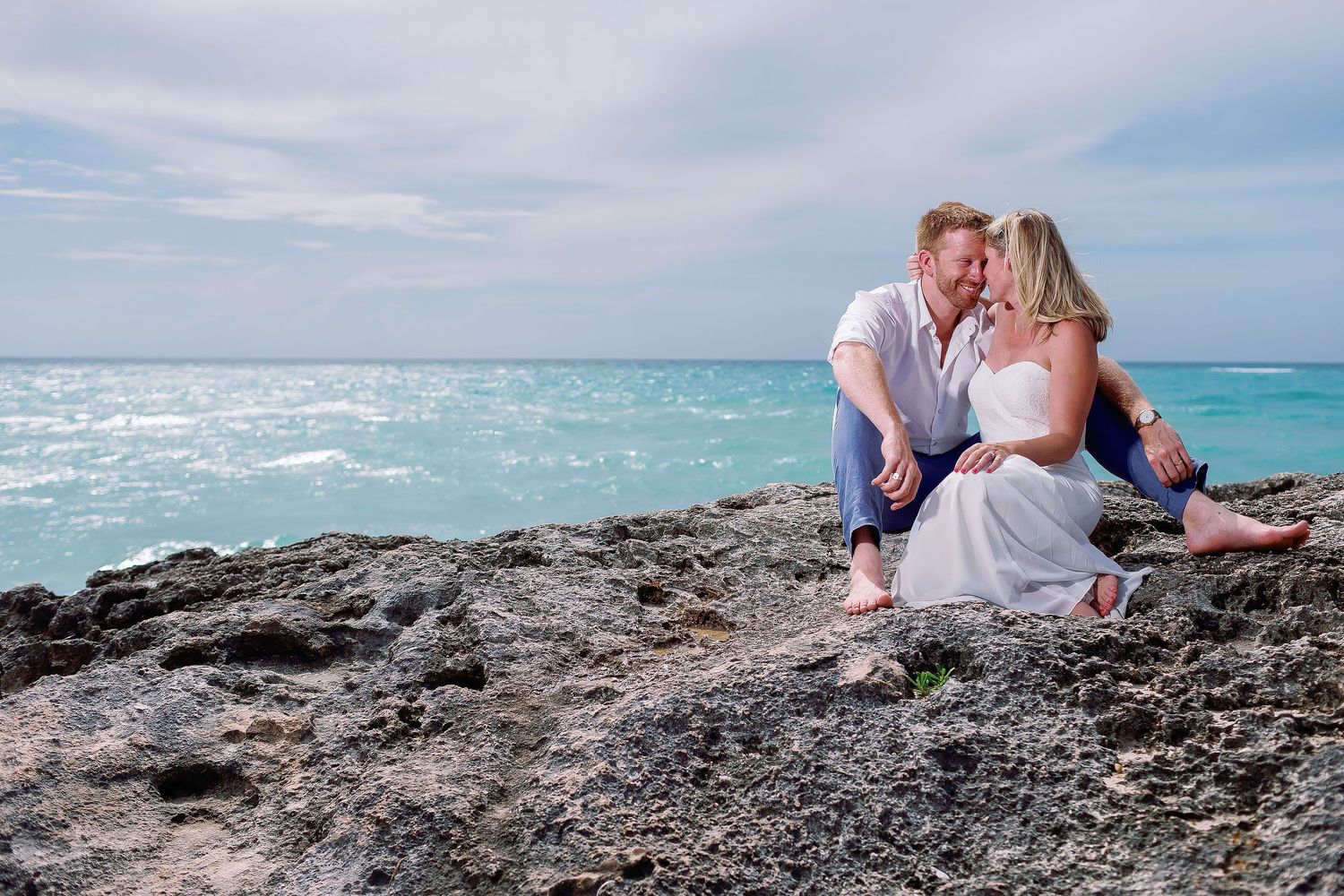 Cressida and Alan sitting together on the rocky coast during their day-after wedding portrait session in Tulum, Mexico.