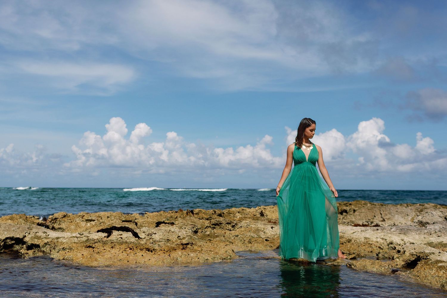 Senior portrait session in Riviera Maya featuring a flowing green dress, rocky shoreline, and turquoise Caribbean waters.