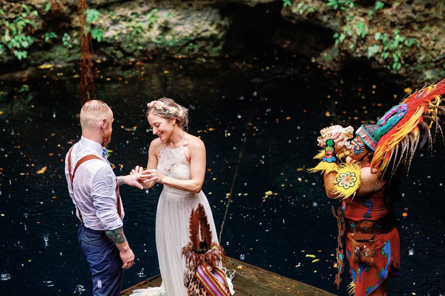 Veronica placing a ring on Jeff’s hand as a ceremonial guide sounds a conch shell during their Maya wedding ceremony at Cenote Hats’uts.
