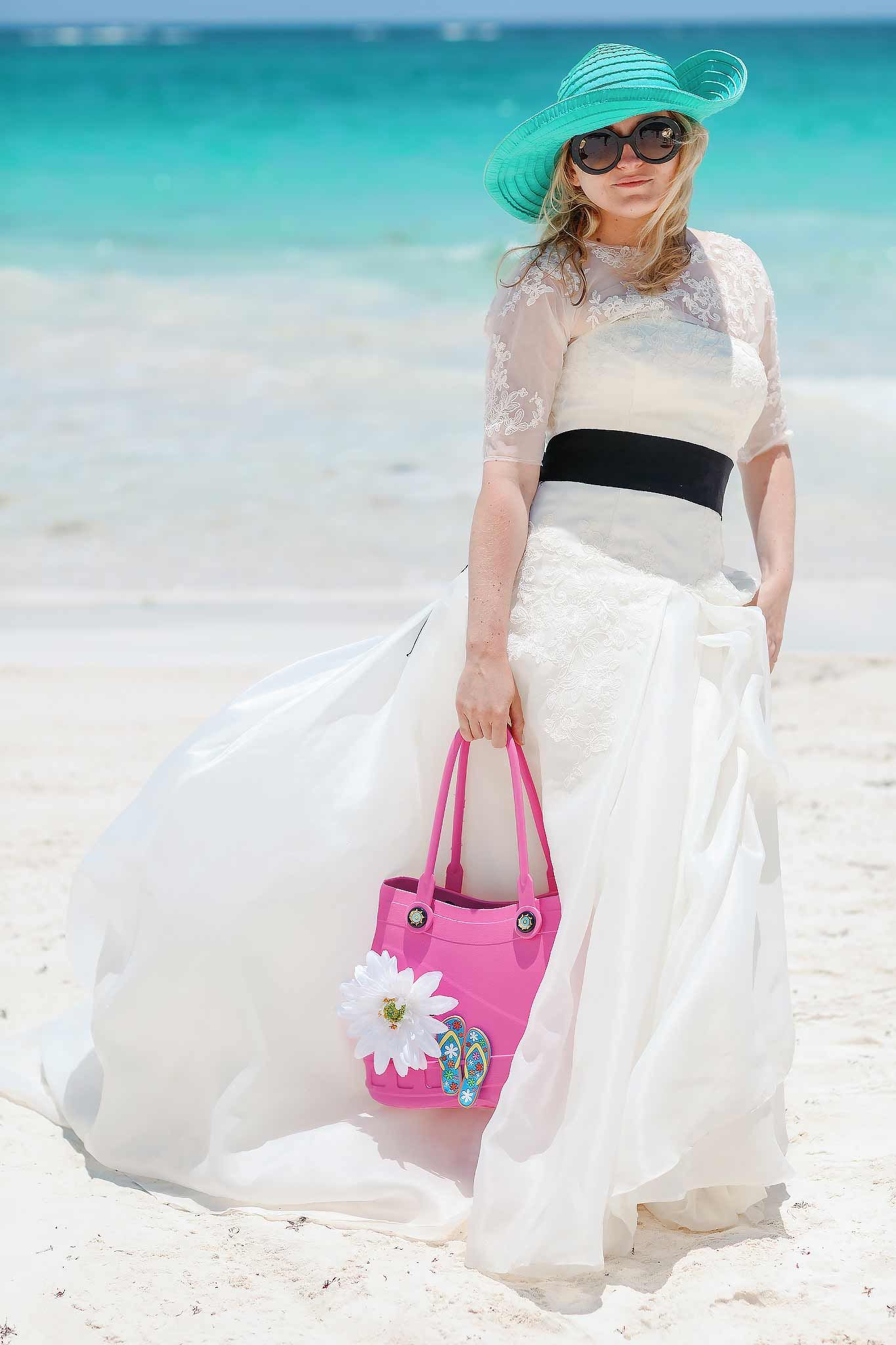 Bride portrait on Cancun beach with turquoise ocean, wearing wedding dress and sun hat during Riviera Maya wedding photography session