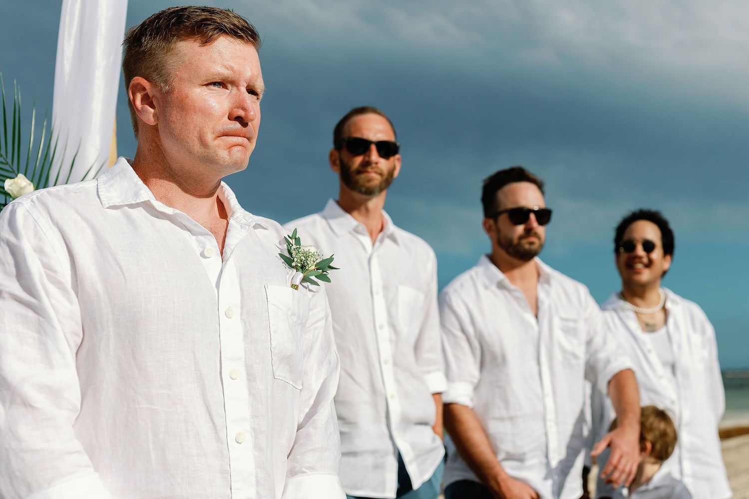 Brian waiting with his wedding party beneath a dramatic sky during the Dreams Sapphire beach ceremony.