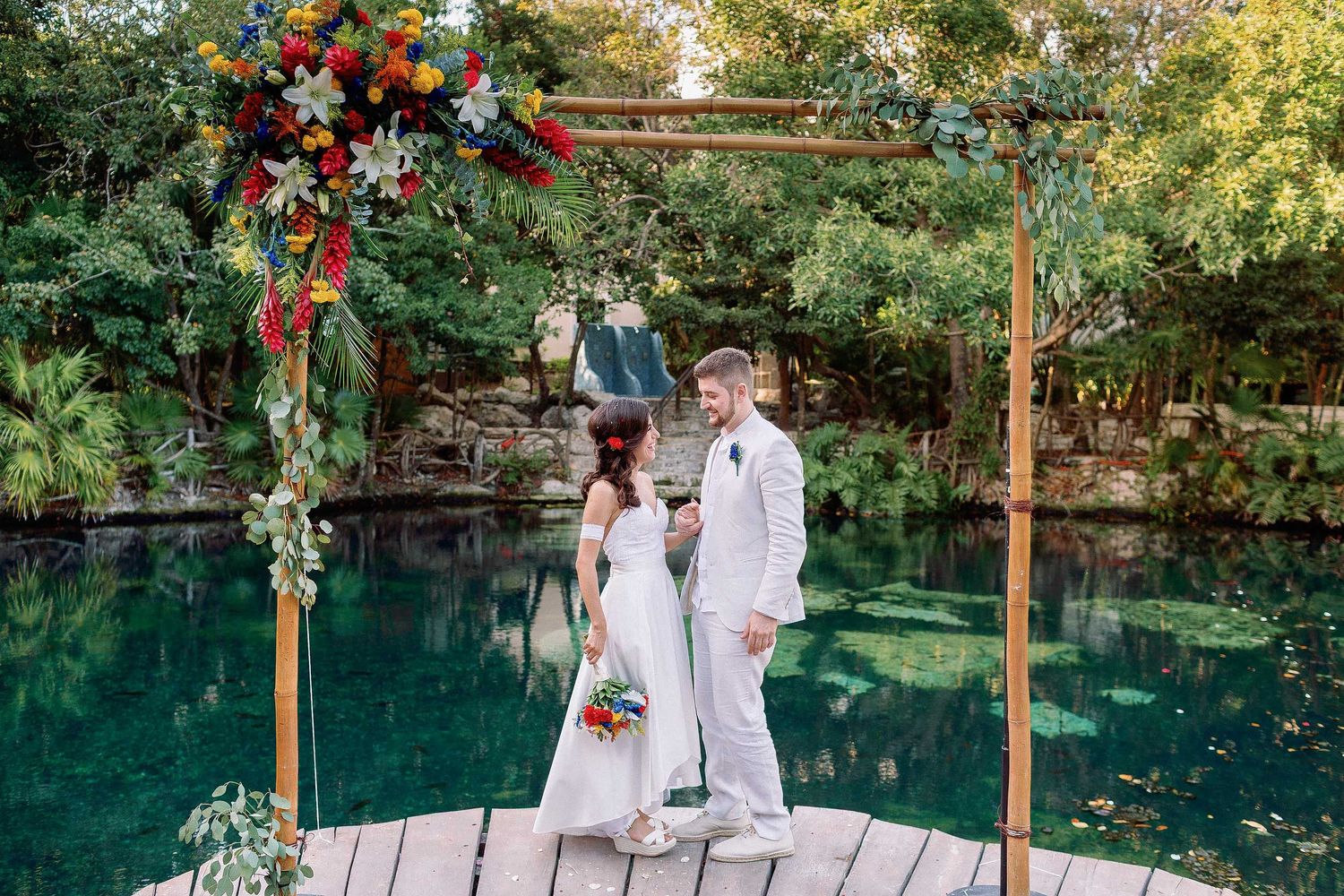 Bride and groom standing beneath a floral arch during a cenote wedding ceremony in Playa del Carmen, Riviera Maya