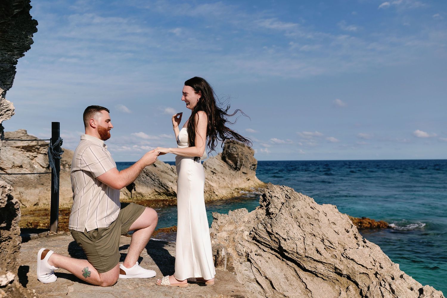 Sam kneels to propose to Alexia on the rocky coast at Punta Sur in Isla Mujeres