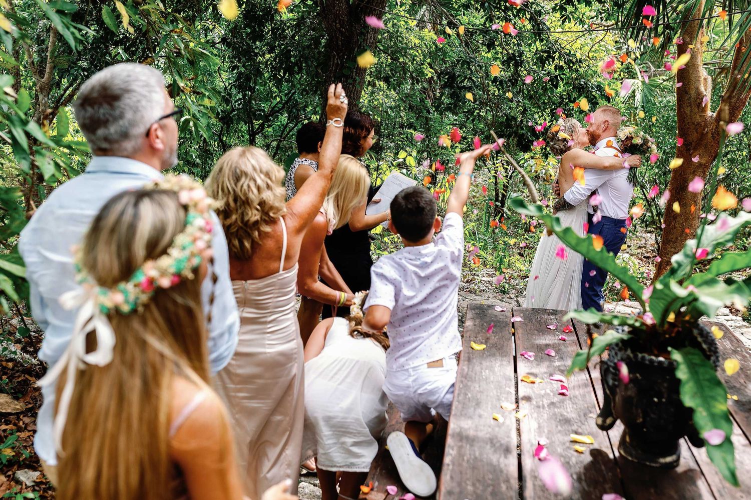 Guests throwing colorful flower petals as Jeff and Veronica kiss after their intimate civil ceremony at Cenote Hats’uts near Playa del Carme