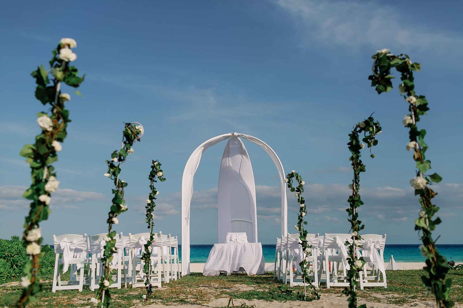 Isla Mujeres beach wedding ceremony setup with white floral arch, chairs, and turquoise Caribbean ocean backdrop