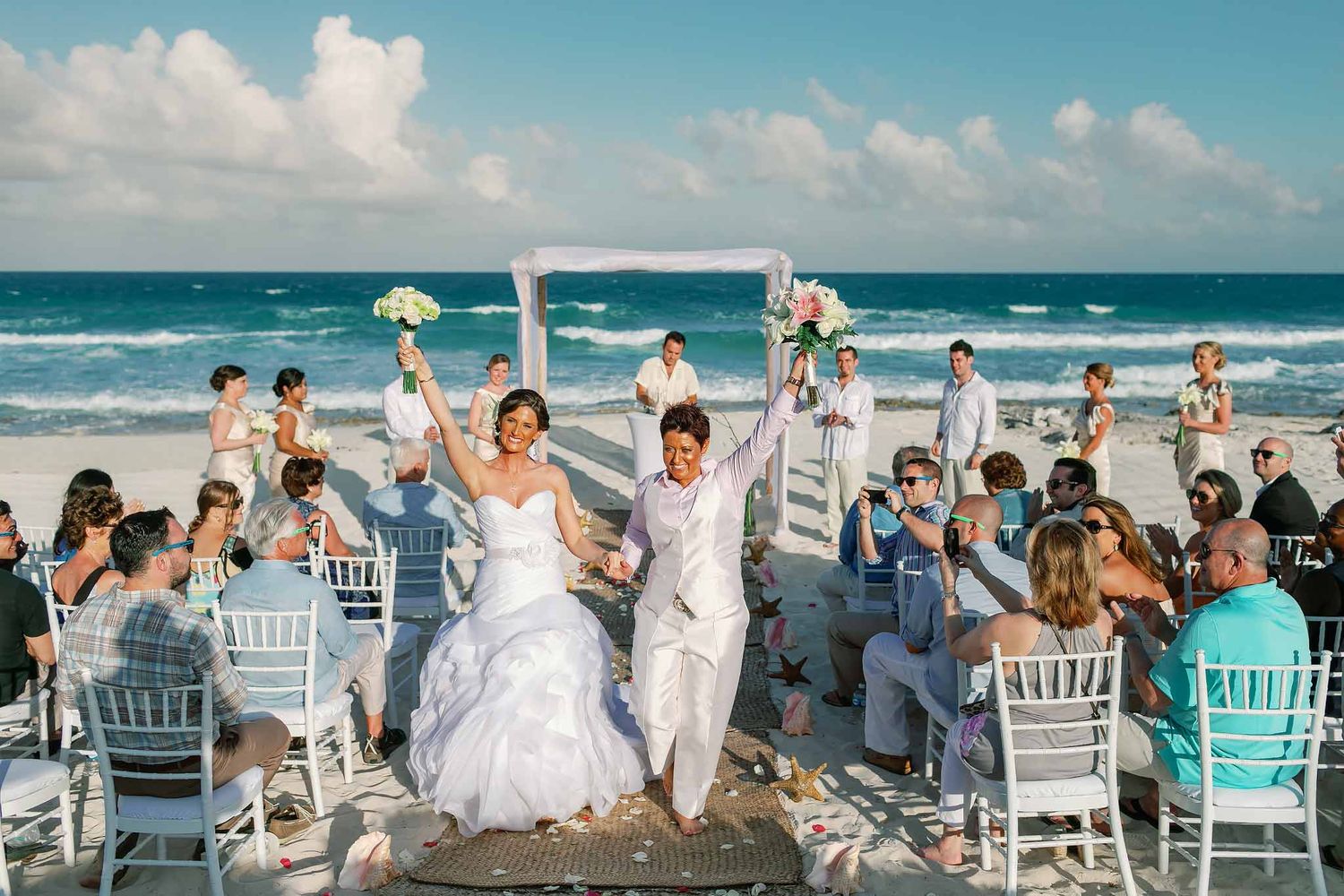 Same-sex couple celebrating wedding ceremony on the beach in Playa del Carmen with ocean backdrop and guests