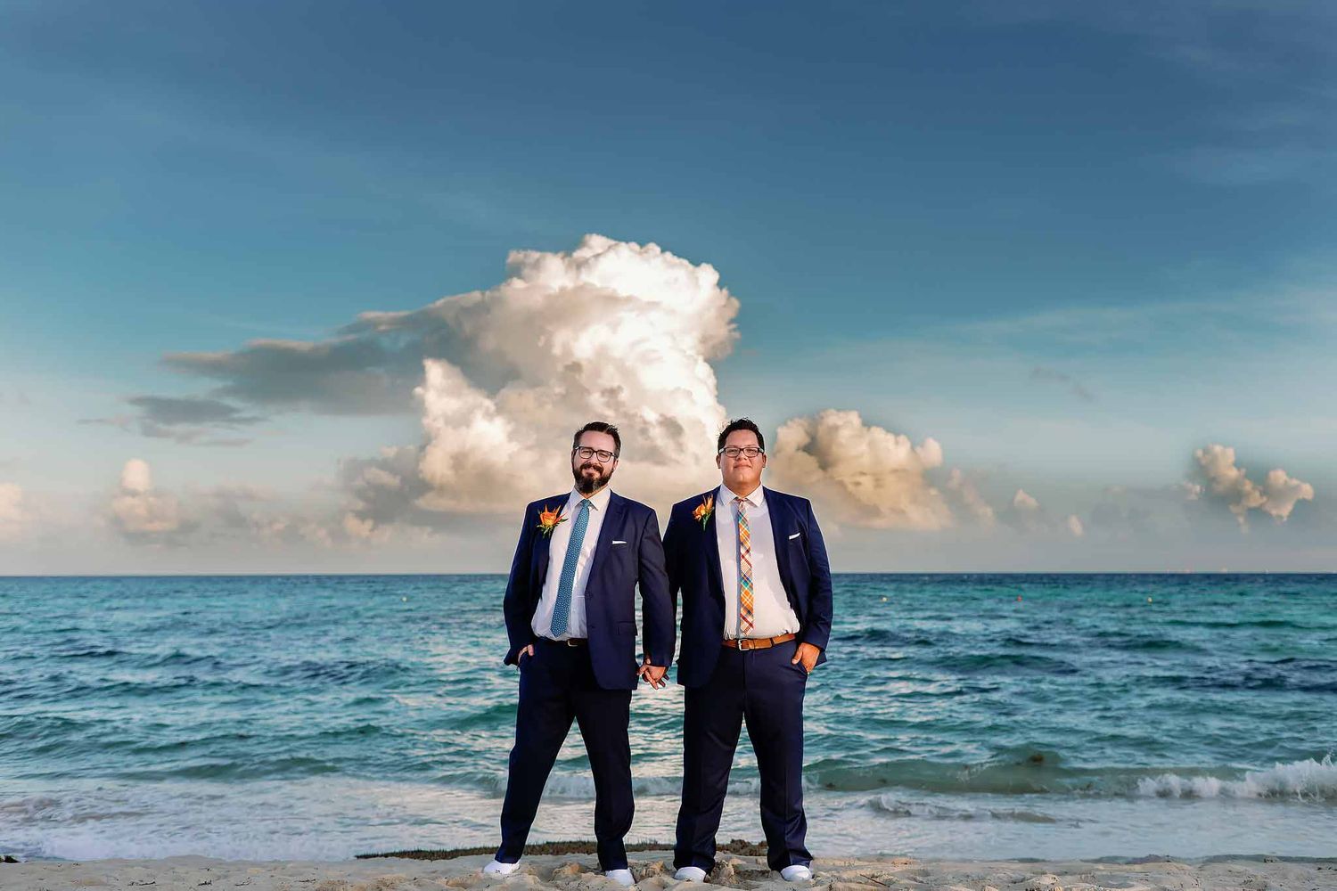 Gay wedding couple portrait on the beach in Costa Mujeres with turquoise ocean and dramatic clouds at sunset.