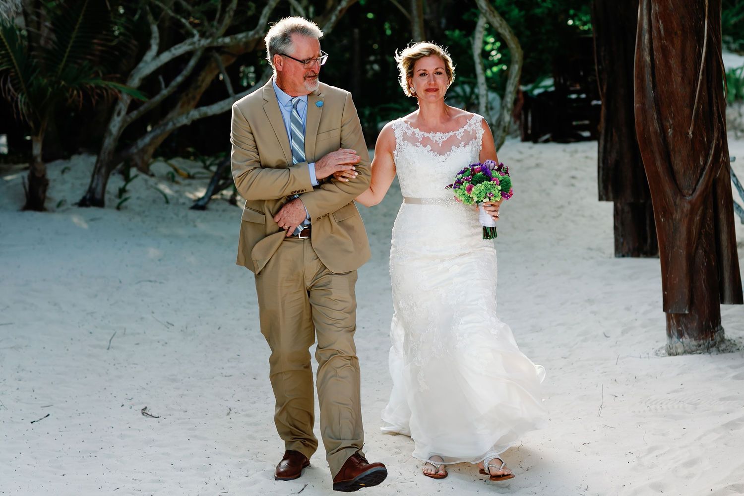 Ashley walks arm in arm with a loved one toward her beach wedding ceremony in Tulum.