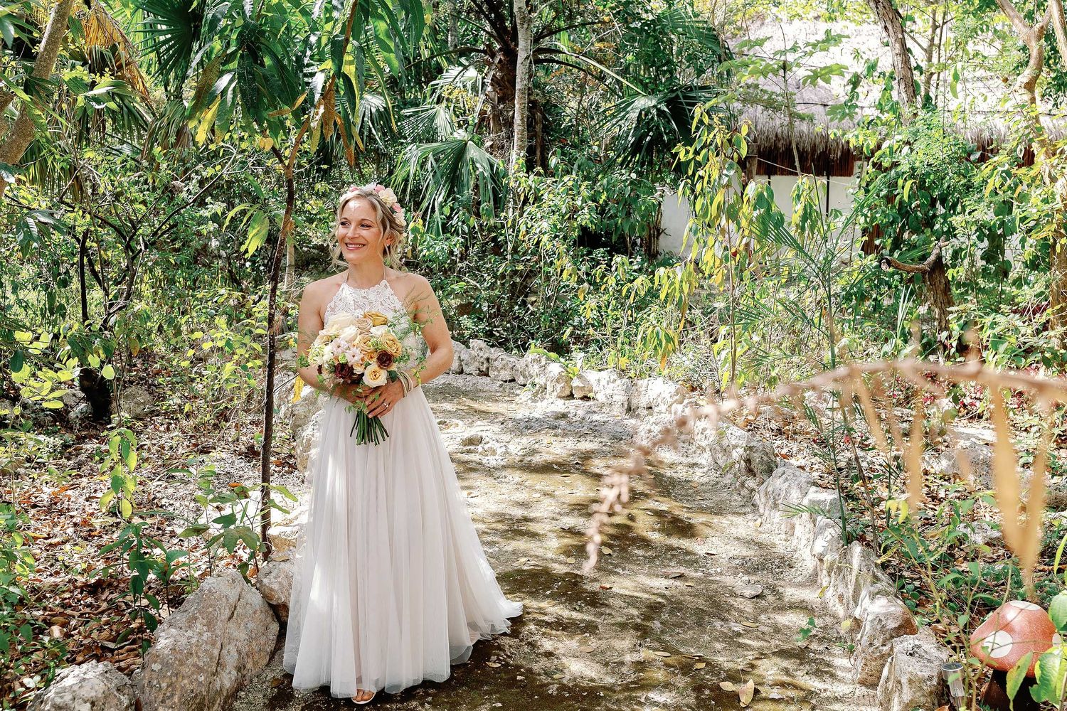 Veronica holding her bouquet on a jungle path before her intimate wedding ceremony at Cenote Hats’uts near Playa del Carmen.