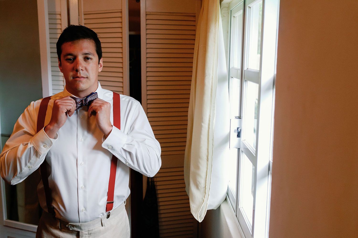 Carlos adjusts his patterned bow tie and red suspenders before his Isla Mujeres wedding.