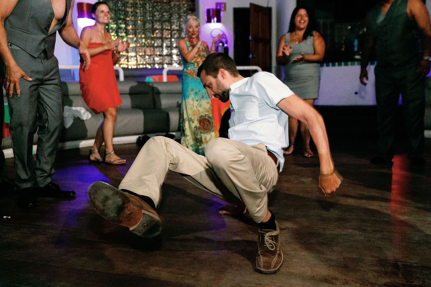 A wedding guest performs an energetic floor dance as the crowd cheers.