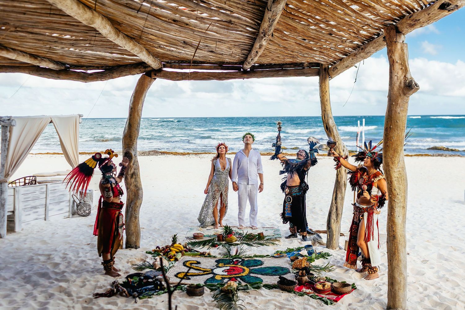 Wide view of Sarah and Evish surrounded by ceremonial participants on a Tulum beach.