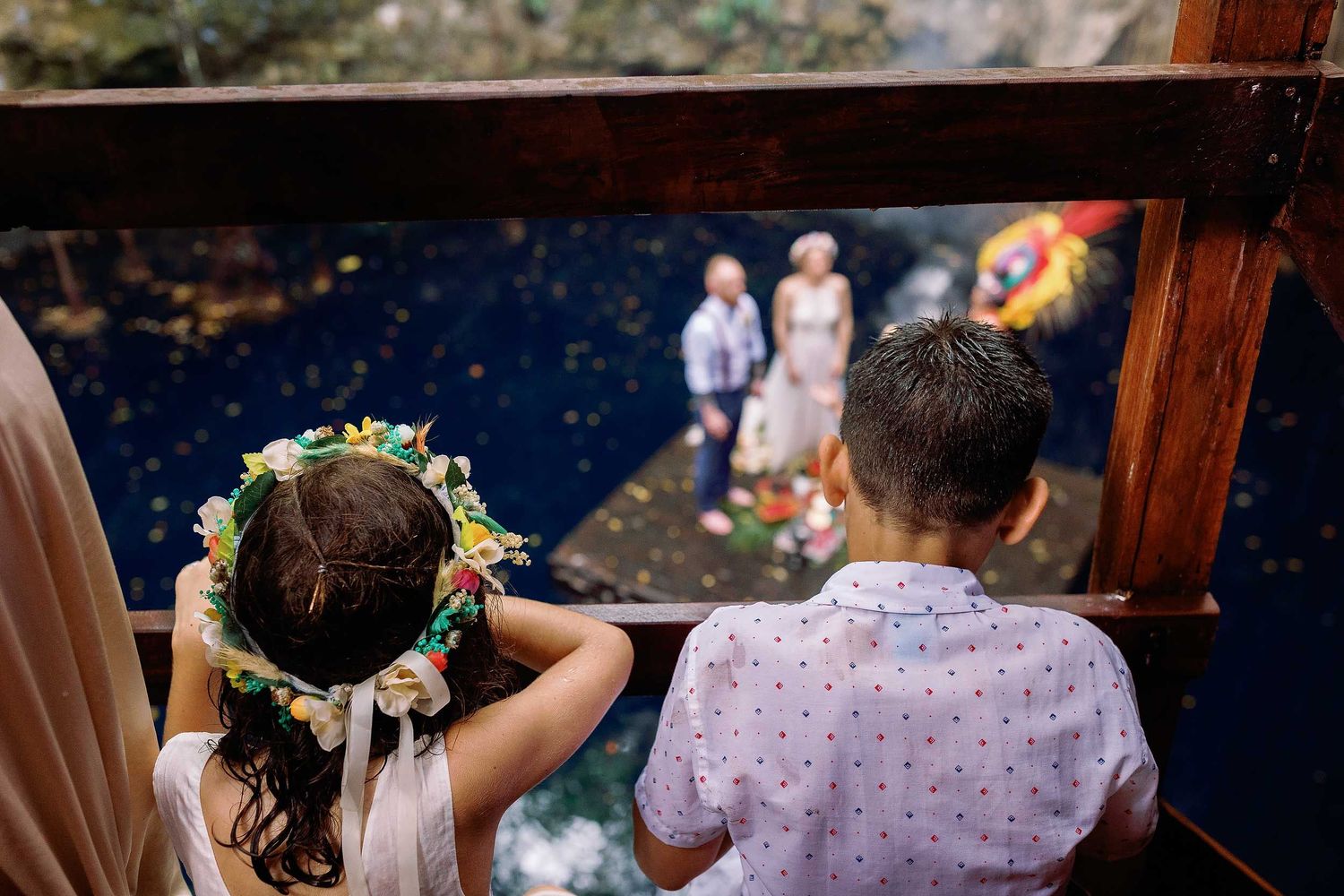 Two young wedding guests watching Jeff and Veronica’s Maya ceremony from a wooden walkway above the water at Cenote Hats’uts.