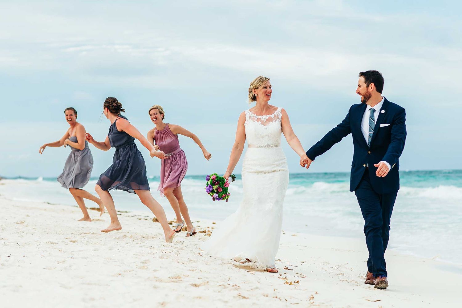 Isla Mujeres wedding photography of bride and groom walking on beach with bridal party and Caribbean ocean backdrop