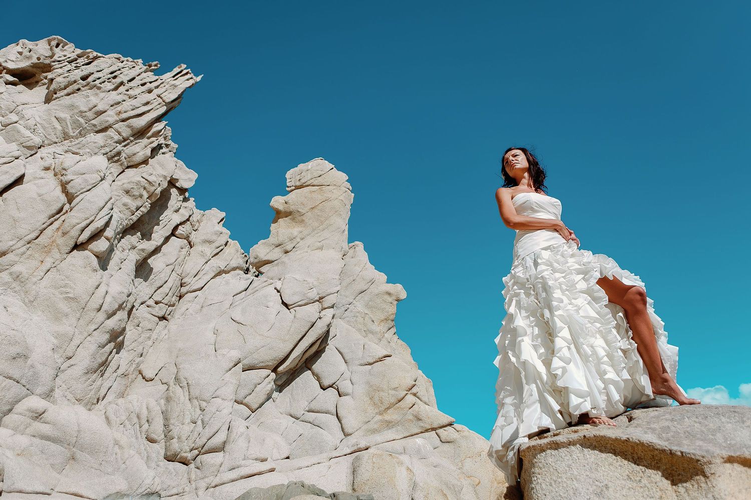 Elegant bride standing on granite cliffs near the famous Los Cabos Arch during a destination wedding portrait session.