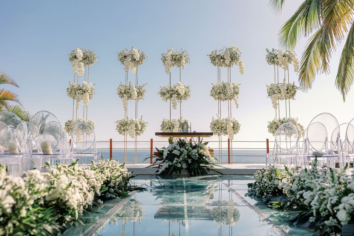 Sophisticated beachfront wedding ceremony design in Puerto Vallarta featuring elevated floral arrangements, tropical palms, and ocean views.
