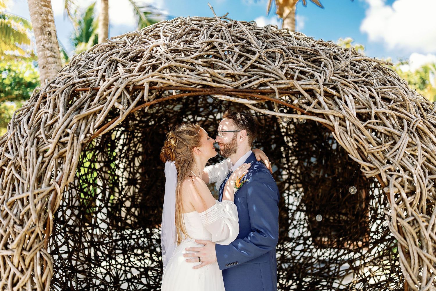 Nicole and Thomas embracing beneath a woven-wood structure during their wedding portraits at Blue Venado in Playa del Carmen.