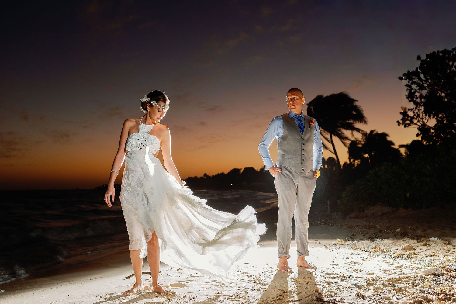 Juliana and Tom pose barefoot on the beach beneath a dramatic Playa del Carmen sunset.