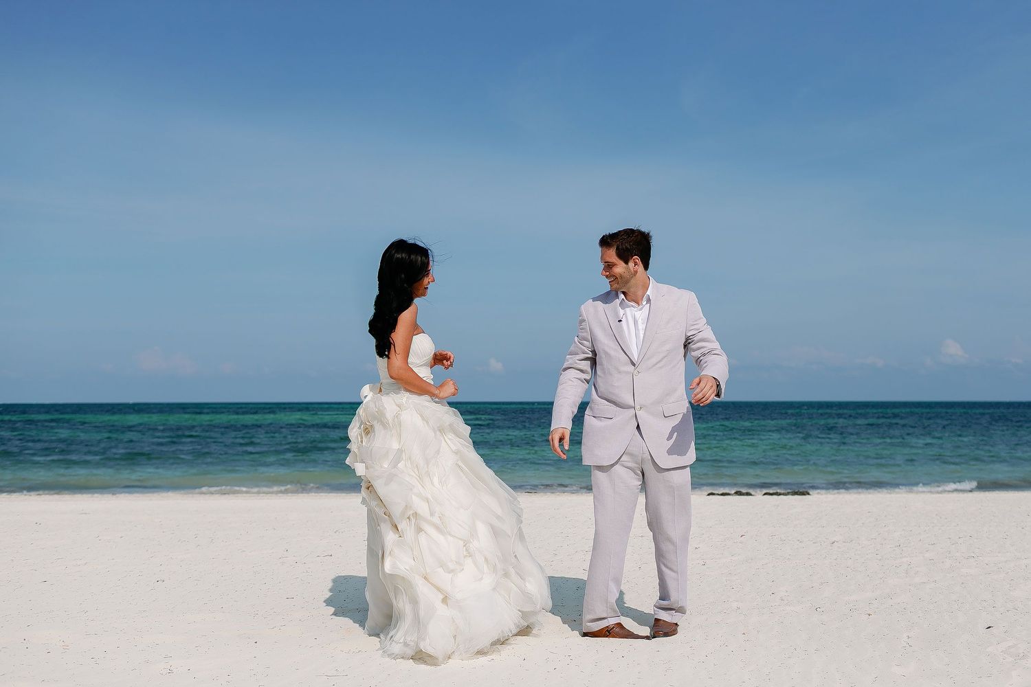 Smiling bride and groom seeing each other during their wedding first look on the white-sand beach at Moon Palace Cancun.