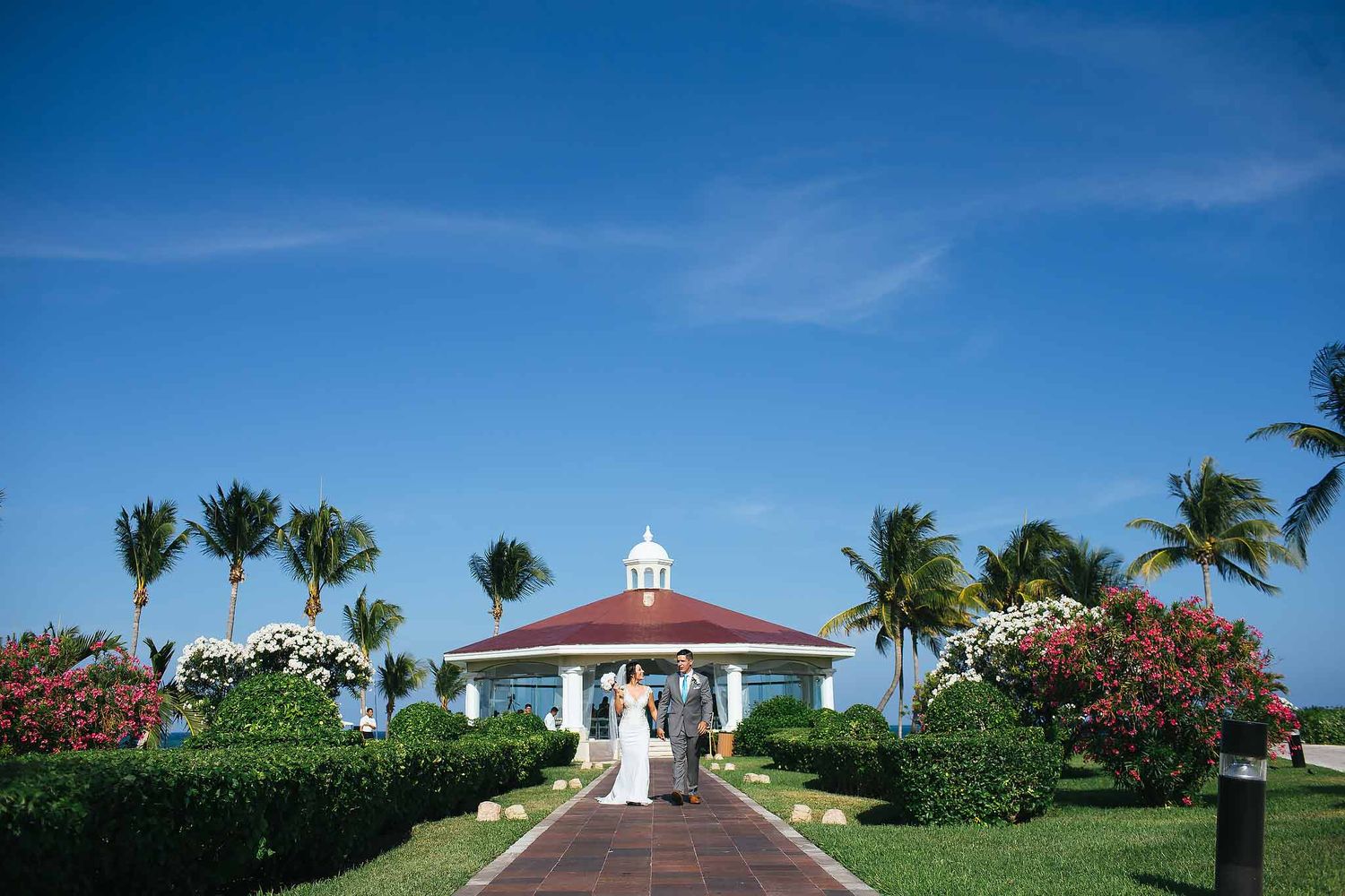 Exterior of Chapel of the Immaculate Conception at Moon Palace Cancun with bride and groom walking in tropical garden